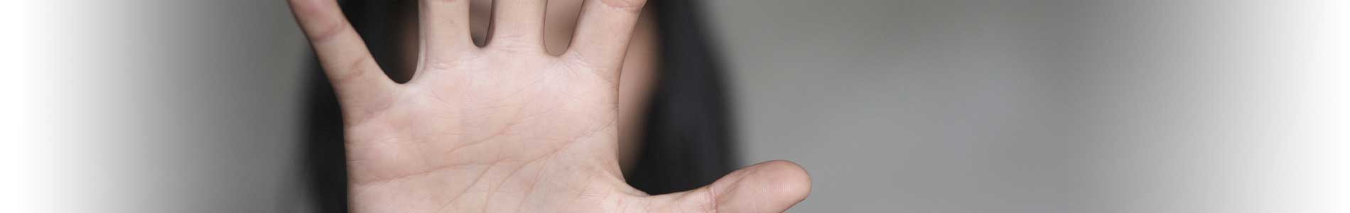 Woman with long dark hair in white shirt with raised hand covering her face to prevent herself from sexual harassment